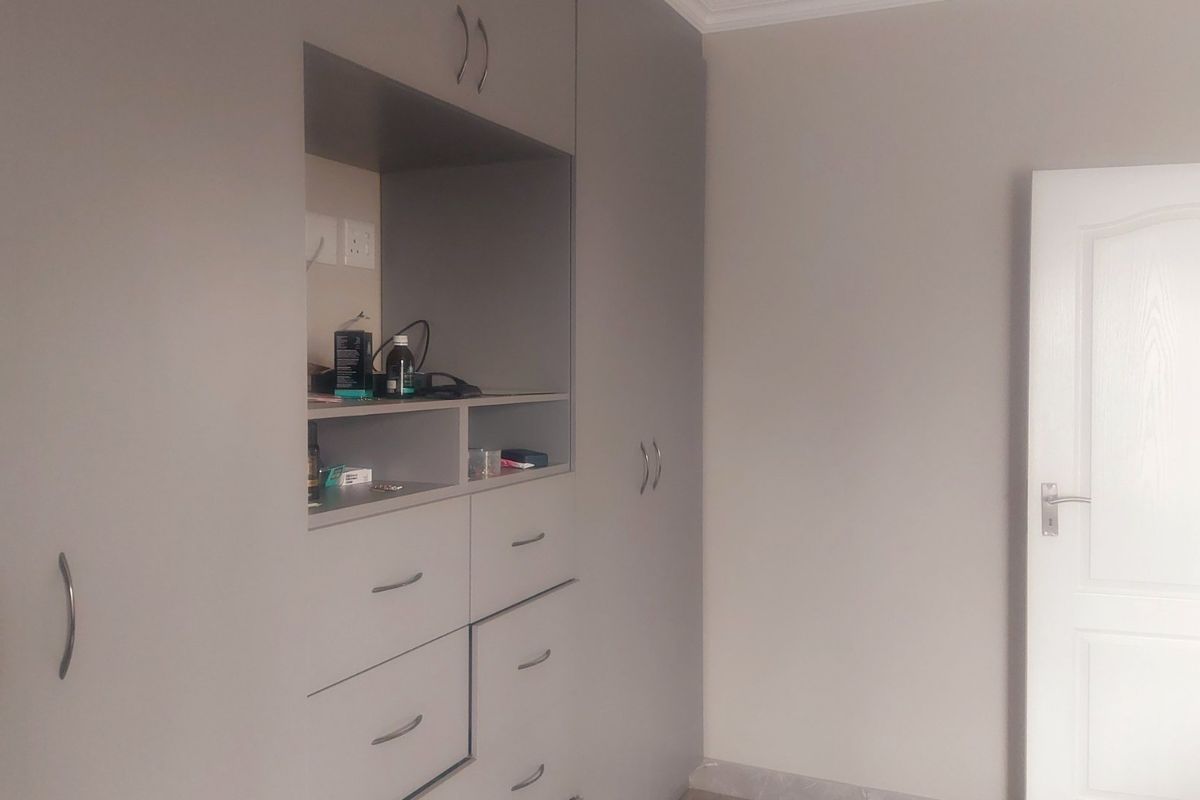 A bedroom featuring modern grey built-in cupboards with integrated shelving, drawers, and a classic panel door.
