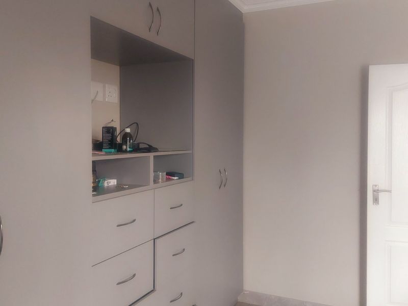 A bedroom featuring modern grey built-in cupboards with integrated shelving, drawers, and a classic panel door.