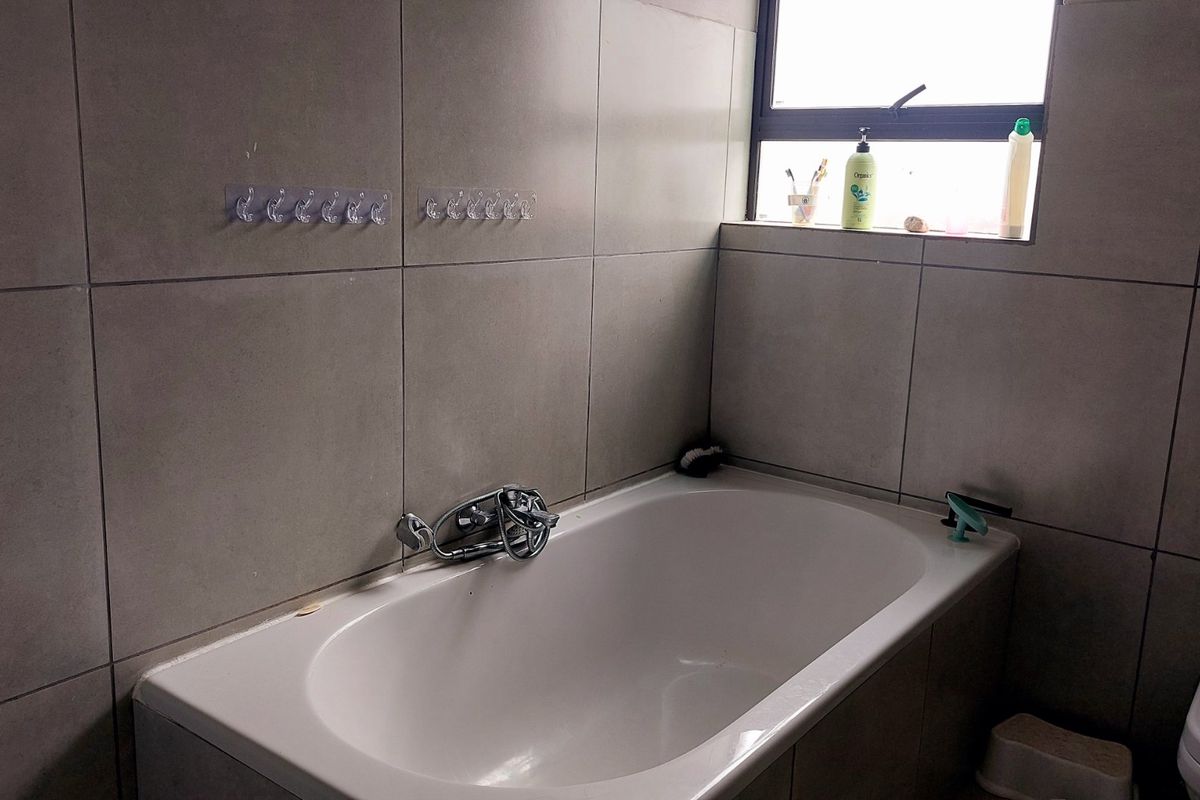 A functional bathroom featuring a built-in bathtub with chrome mixer tap, ceramic wall tiles, and a toilet.