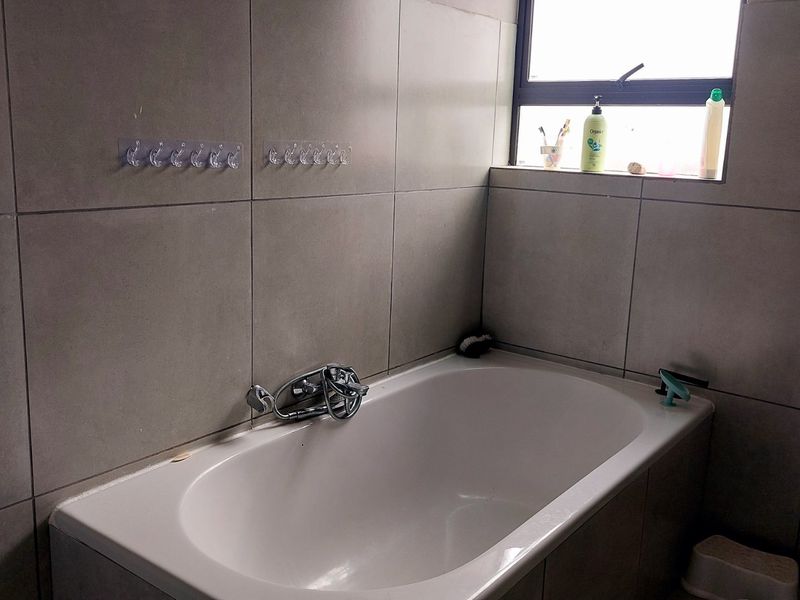 A functional bathroom featuring a built-in bathtub with chrome mixer tap, ceramic wall tiles, and a toilet.