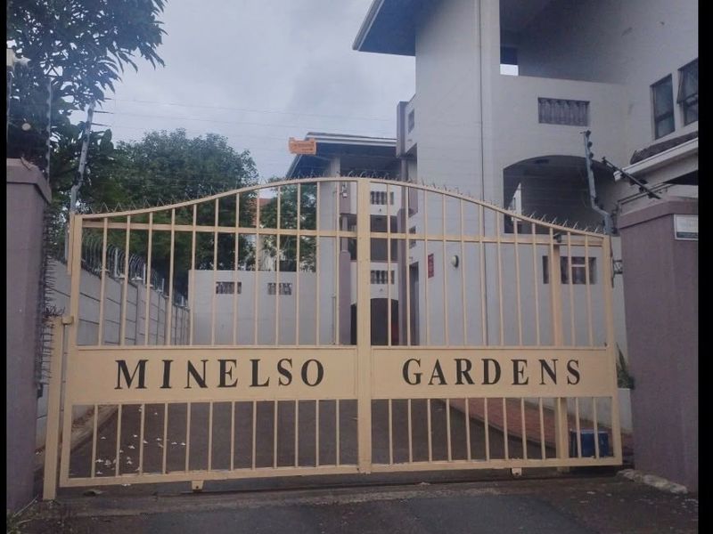 Front entrance view of Minelso Gardens apartment complex featuring a secure gated access point and perimeter walling.