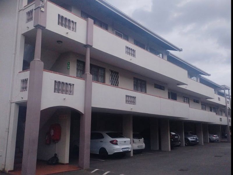 Exterior view of an apartment complex featuring covered ground-level parking bays and upper-level balconies with concrete balustrades.