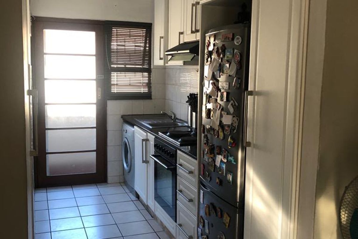 A functional galley-style kitchen featuring white cabinetry, built-in oven and hob, tiled flooring, and direct access to an outdoor area.