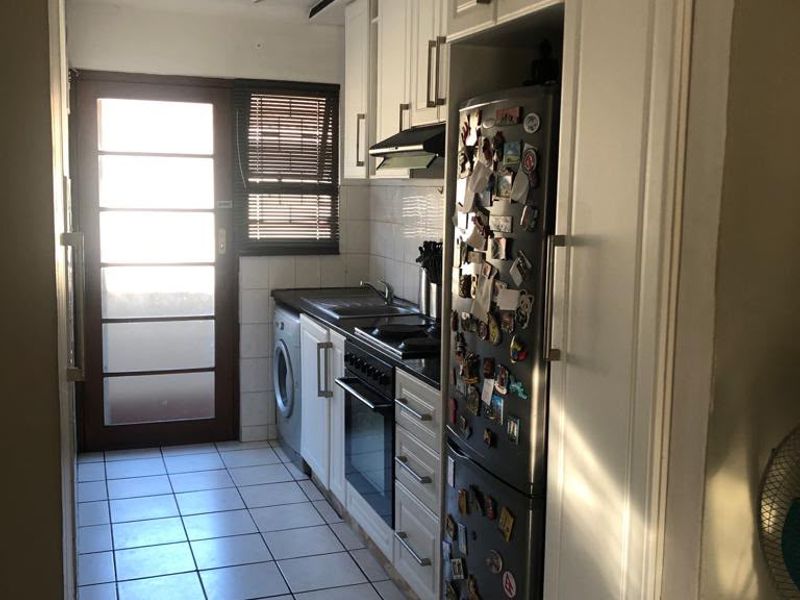 A functional galley-style kitchen featuring white cabinetry, built-in oven and hob, tiled flooring, and direct access to an outdoor area.
