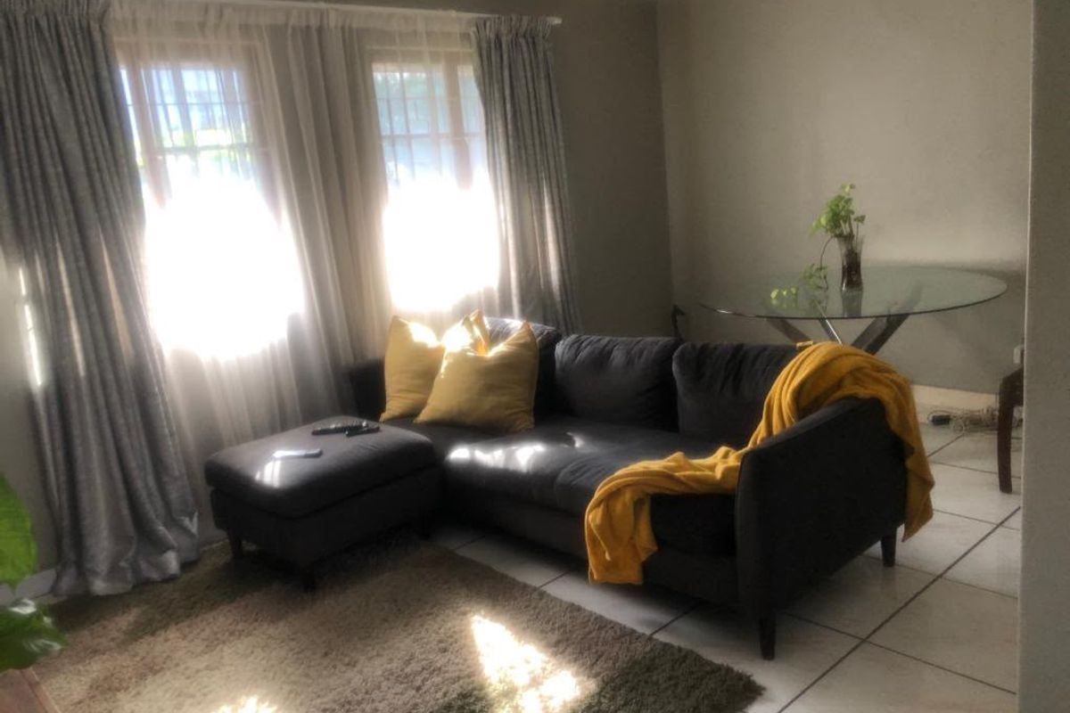 A living room area featuring tiled flooring and large windows with curtain rails, providing natural light to the space.