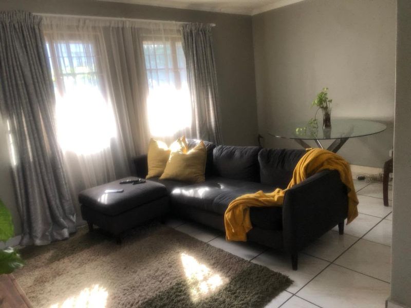 A living room area featuring tiled flooring and large windows with curtain rails, providing natural light to the space.