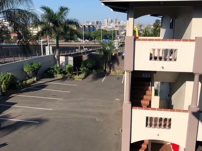 Exterior view of the apartment complex showing the rear staircase, parking area, and surrounding urban landscape.