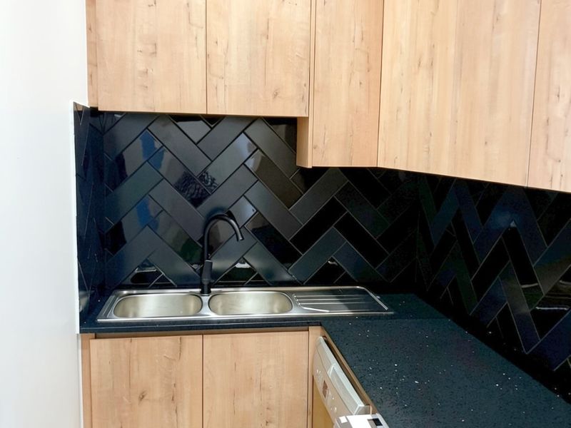 Modern kitchen featuring light wood cabinetry, a striking black herringbone tile backsplash, black stone countertops, and a sleek black faucet.