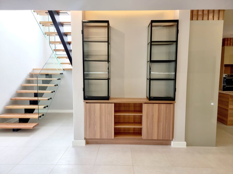 Modern living area featuring a striking floating staircase with glass balustrade and custom built-in timber cabinetry with fluted glass display units.
