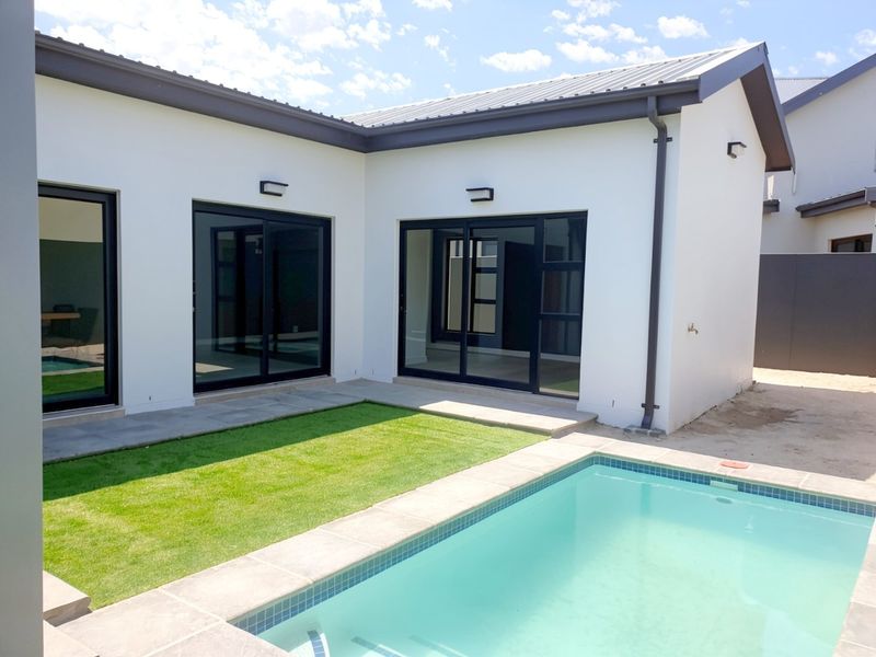 A modern rear exterior view featuring a swimming pool, manicured lawn, and large sliding glass doors providing seamless indoor-outdoor flow.