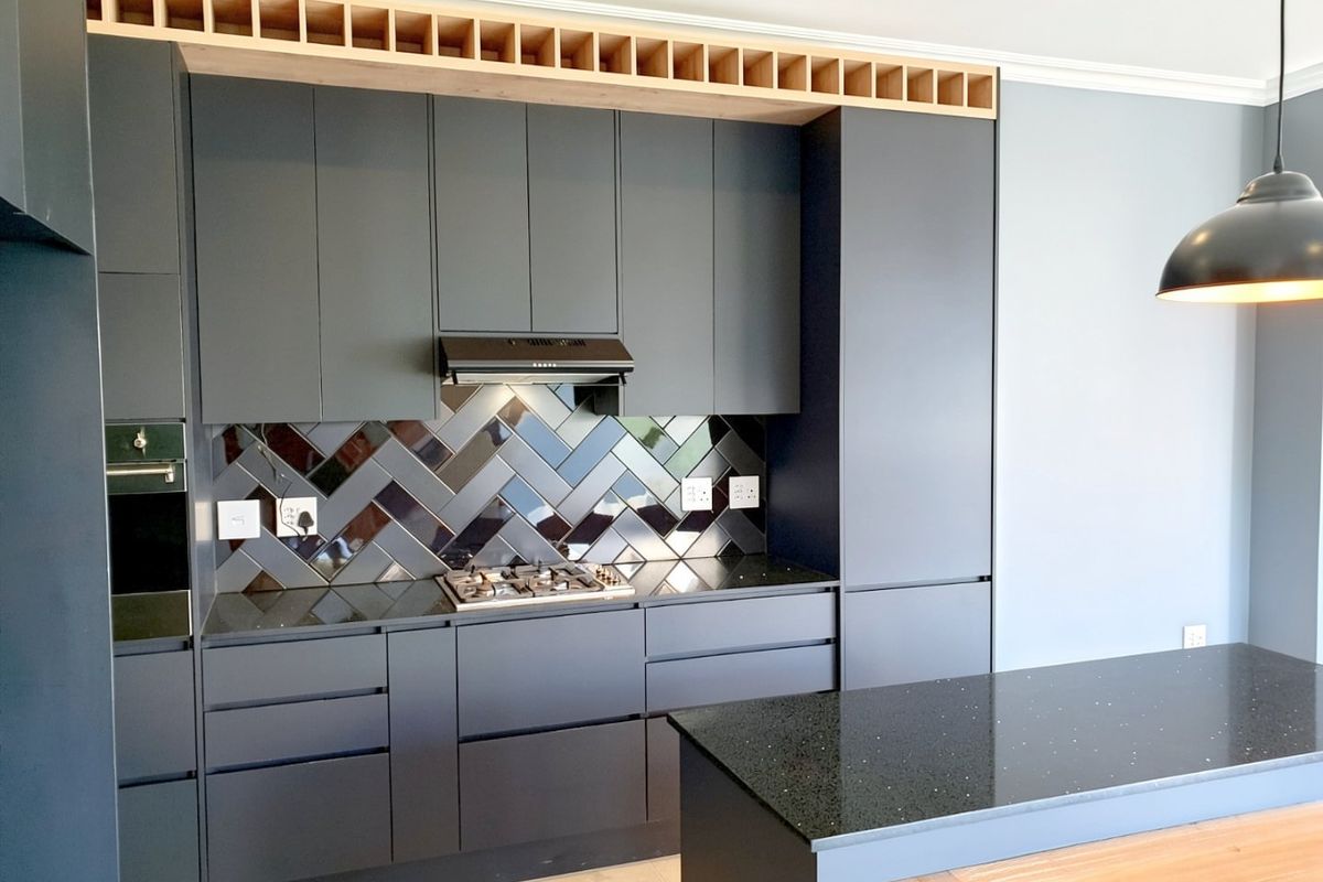 Modern kitchen featuring dark cabinetry, a herringbone tile splashback, stone countertops, a gas hob, and a functional kitchen island with integrated storage.
