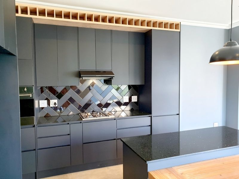 Modern kitchen featuring dark cabinetry, a herringbone tile splashback, stone countertops, a gas hob, and a functional kitchen island with integrated storage.