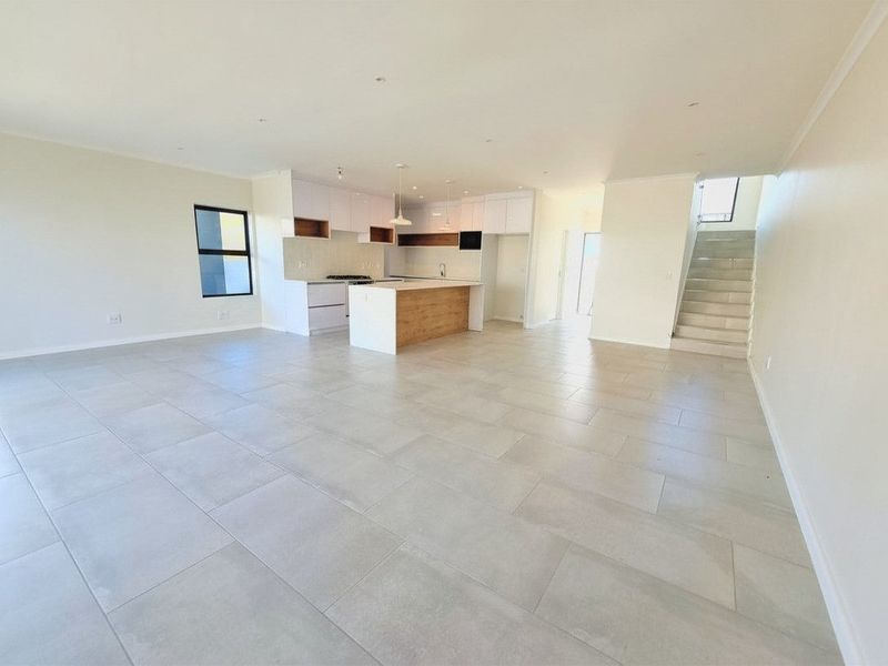 Spacious open-plan living area featuring a modern kitchen with a central island, tiled flooring, and a staircase leading to the upper level.