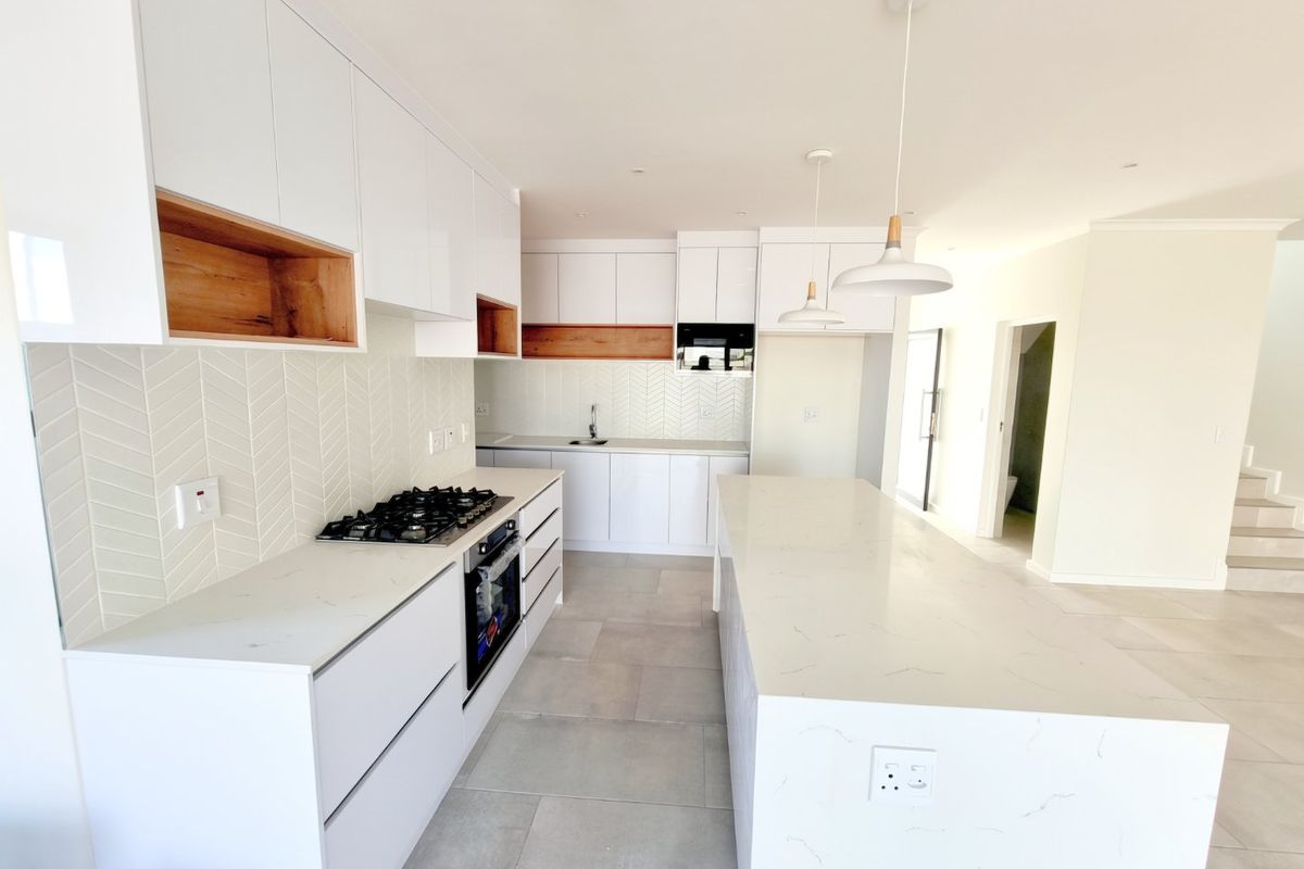 Modern kitchen featuring white cabinetry, stone countertops, a central island, gas hob, built-in oven, and stylish herringbone tile backsplash.
