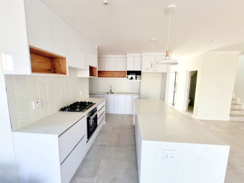 Modern kitchen featuring white cabinetry, stone countertops, a central island, gas hob, built-in oven, and stylish herringbone tile backsplash.