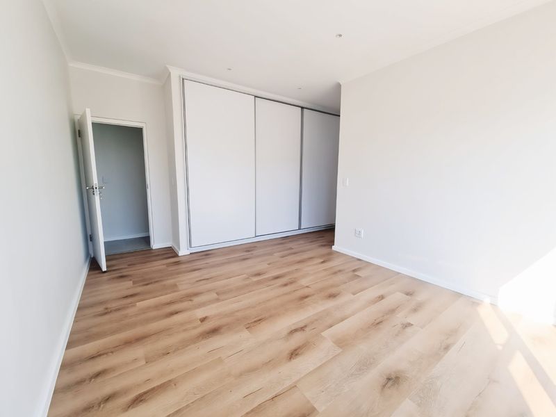 A bright, vacant bedroom featuring modern laminate flooring, recessed lighting, and a large built-in sliding door wardrobe.
