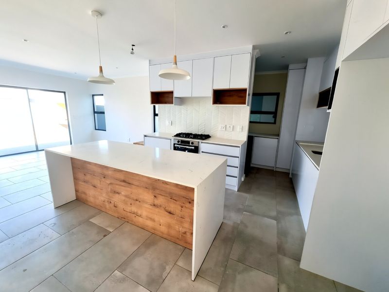 Modern open-plan kitchen featuring a large island with wood-grain detailing, quartz countertops, gas hob, and herringbone backsplash, flowing into a bright living area.