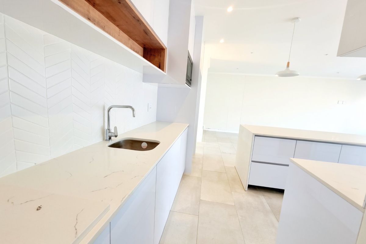 Modern kitchen featuring white cabinetry, stone countertops, herringbone tile backsplash, and integrated lighting, presented in a clean, minimalist, and vacant state.