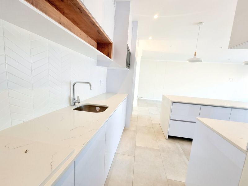 Modern kitchen featuring white cabinetry, stone countertops, herringbone tile backsplash, and integrated lighting, presented in a clean, minimalist, and vacant state.