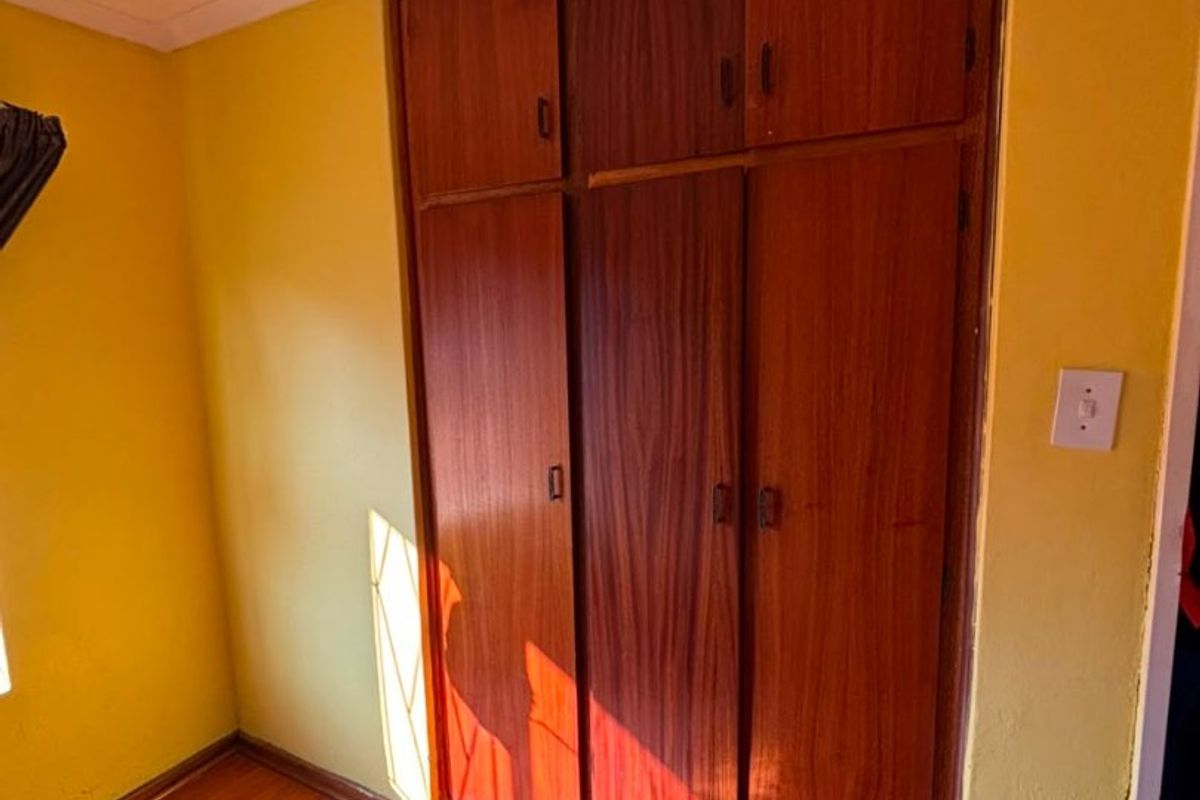 A bedroom featuring built-in wooden cupboards, laminate flooring, and coved ceilings, offering a functional space ready for cosmetic updates.