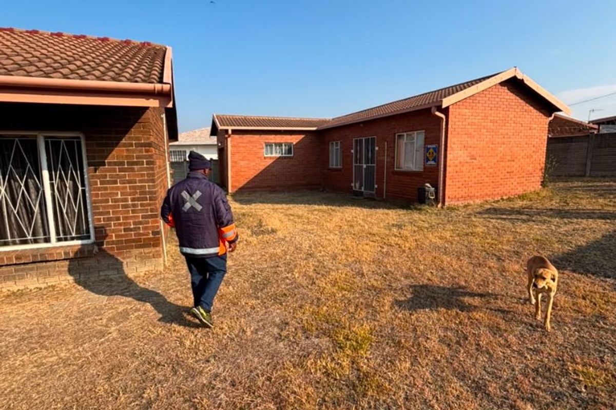 A view of the rear exterior of the house featuring brick construction, tiled roofing, and security bars on the windows.