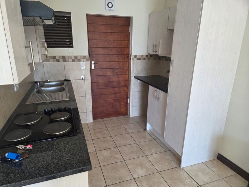 A functional kitchen featuring built-in cabinetry, granite countertops, an electric hob with extractor fan, and tiled flooring.
