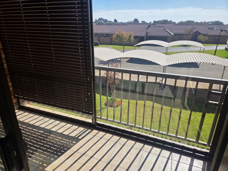 A private balcony featuring tiled flooring and a metal balustrade, offering an elevated view of the complex parking area and surrounding grounds.