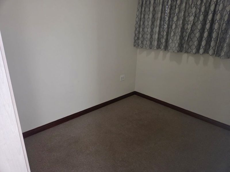 An empty bedroom featuring neutral wall paint, carpeted flooring, and dark wood-tone skirting boards.