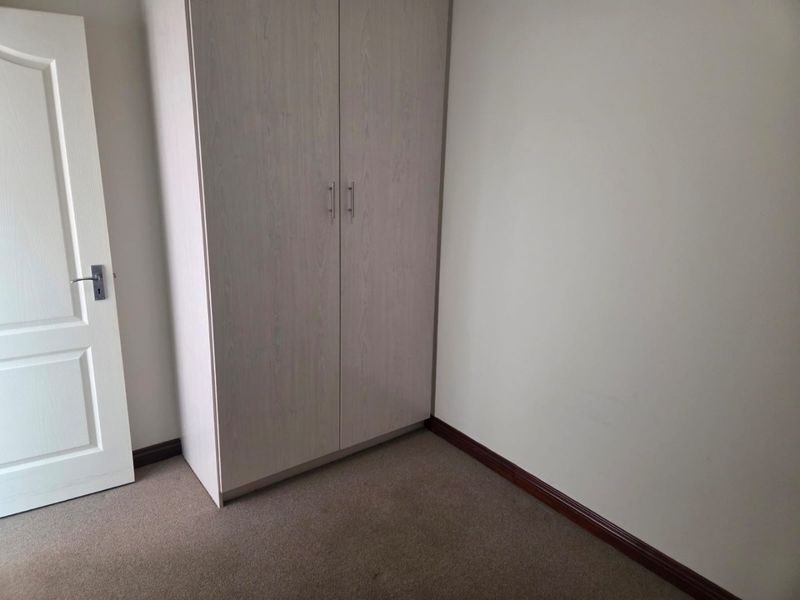 A clean, empty bedroom featuring neutral walls, carpeted flooring, and a built-in wardrobe with light wood-grain finish.
