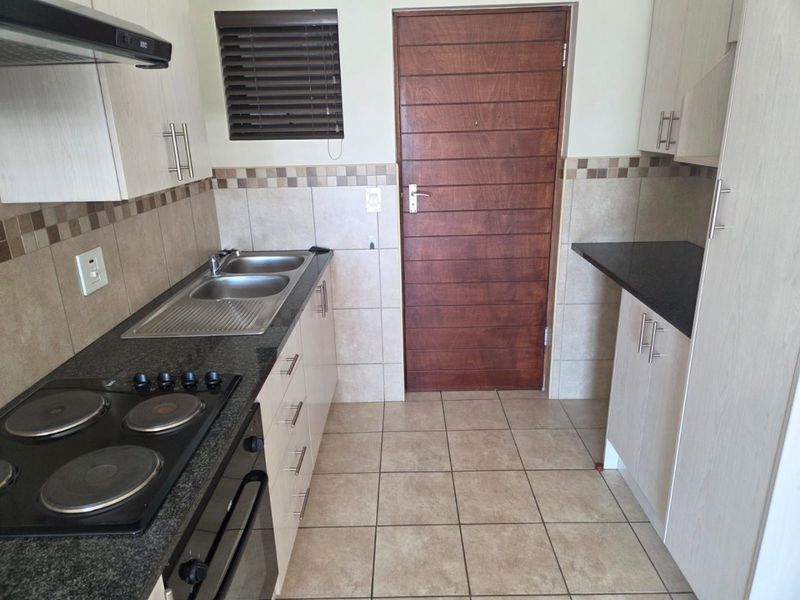 A functional kitchen featuring light-toned cabinetry, granite countertops, a built-in electric hob and oven, and tiled finishes throughout.