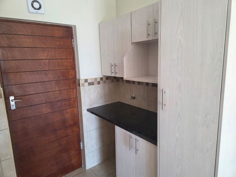 A functional laundry area featuring built-in light wood cabinetry, a durable granite countertop, and tiled backsplash with dedicated plumbing connections.