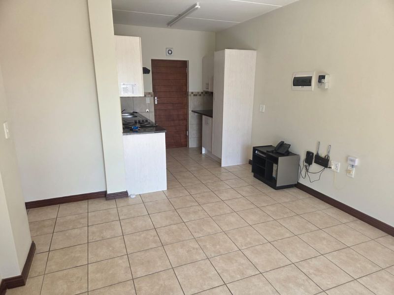 Open-plan living area featuring tiled flooring and a compact kitchen with built-in cabinetry and laminate countertops.
