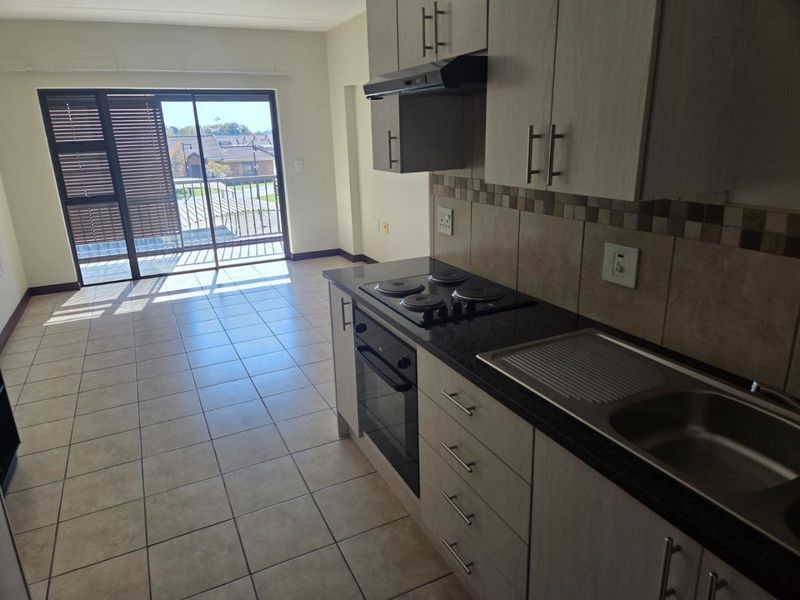 Open-plan kitchen and living area featuring tiled floors, built-in cabinetry with granite countertops, and a sliding door leading to a balcony.