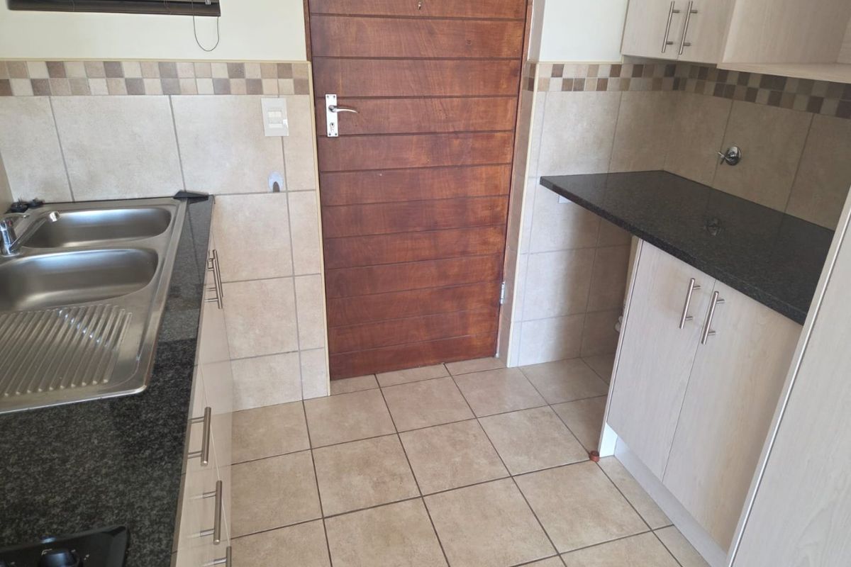 A functional kitchen featuring granite countertops, double stainless steel sink, tiled backsplash, and ample built-in cabinetry with tiled flooring.