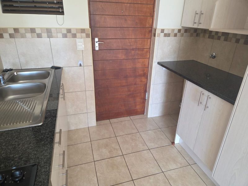 A functional kitchen featuring granite countertops, double stainless steel sink, tiled backsplash, and ample built-in cabinetry with tiled flooring.