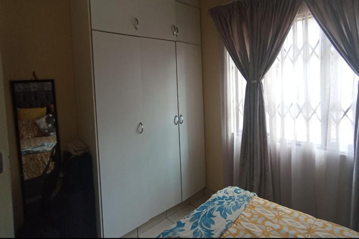 A bedroom featuring built-in cupboards, tiled flooring, and a window fitted with a security gate.