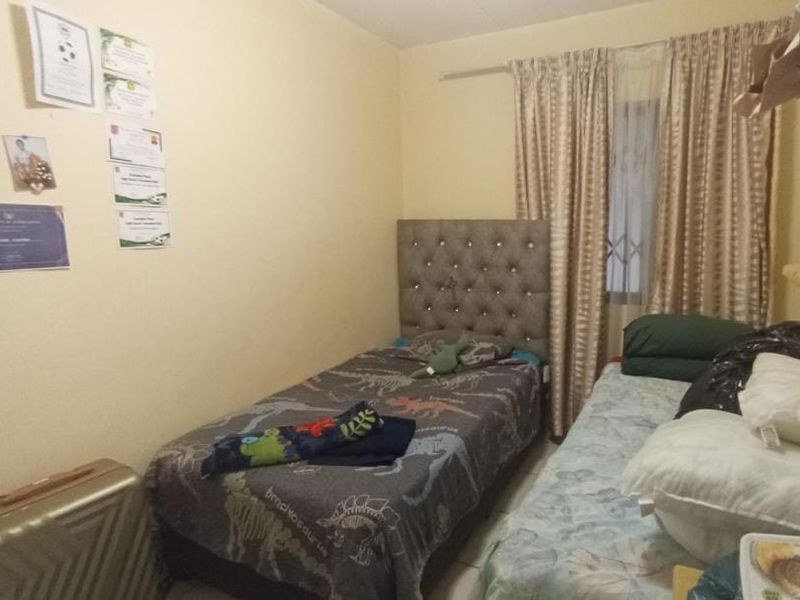 A compact bedroom featuring neutral wall finishes, a curtain rail, and a security gate on the window.