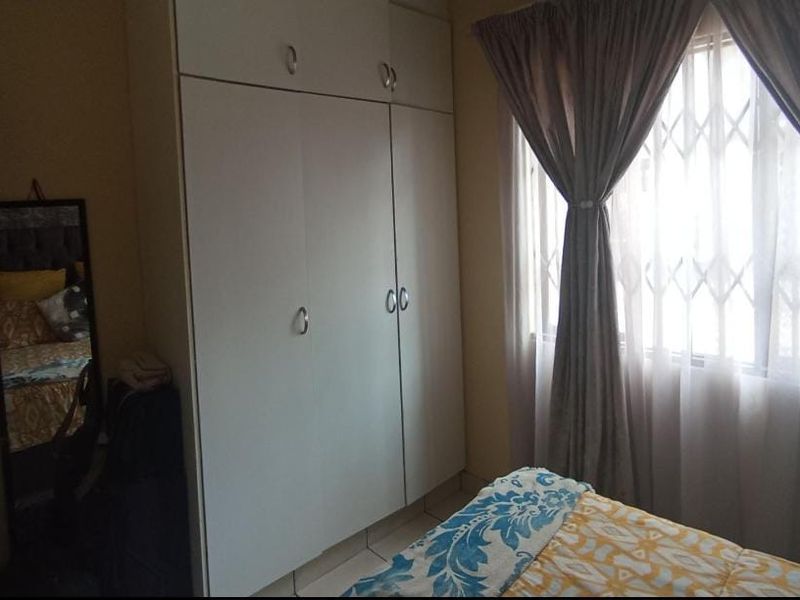 A bedroom featuring built-in cupboards, tiled flooring, and a window fitted with a security gate.