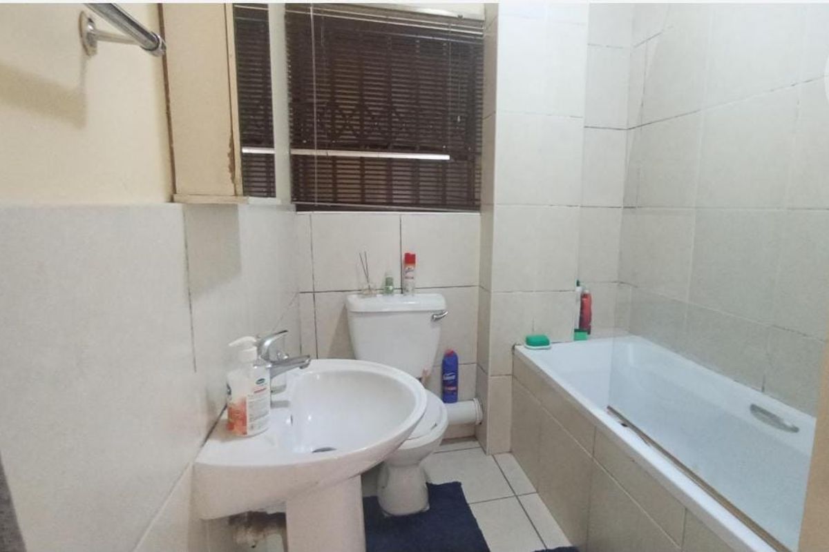 A compact bathroom featuring a pedestal basin, toilet, and bathtub with full-height wall tiling and tiled flooring.