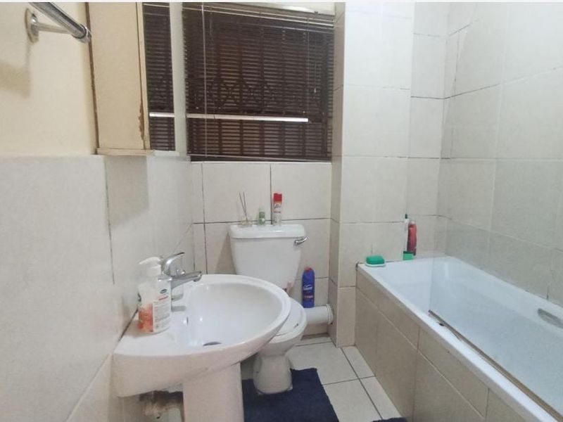 A compact bathroom featuring a pedestal basin, toilet, and bathtub with full-height wall tiling and tiled flooring.