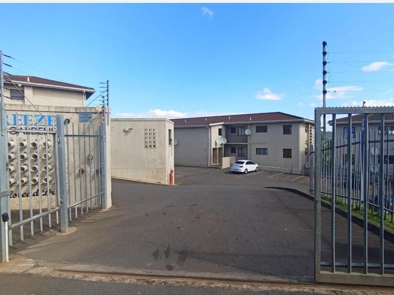 View of the apartment complex entrance featuring a secure gated access point, asphalt driveway, and designated parking area.