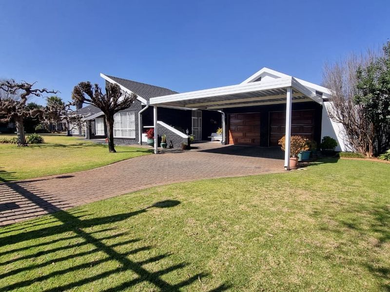 Front view of the property featuring a paved driveway, double garage, and a covered carport set within a well-maintained garden.