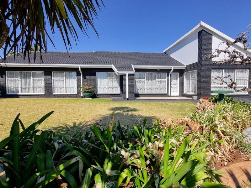 Rear view of a well-maintained single-story house featuring a dark painted brick facade, tiled roof, and large windows overlooking a spacious garden.