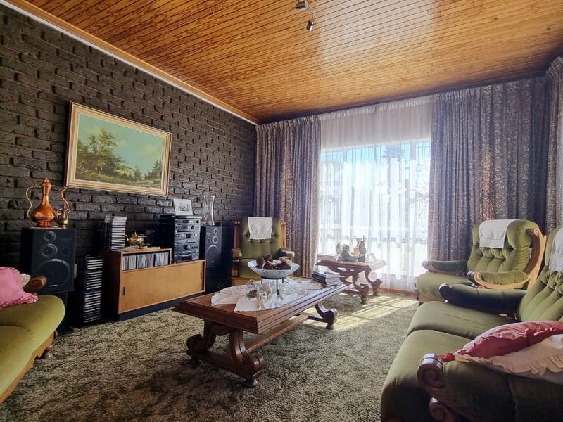 A traditional living room featuring an exposed brick feature wall, timber-clad ceiling, and large windows allowing for natural light.