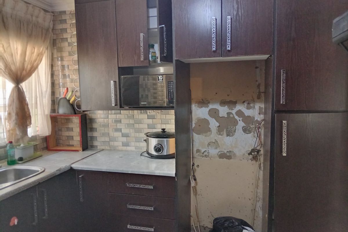 A kitchen featuring dark wood cabinetry and tiled backsplash, currently requiring repairs to the wall and appliance housing area.