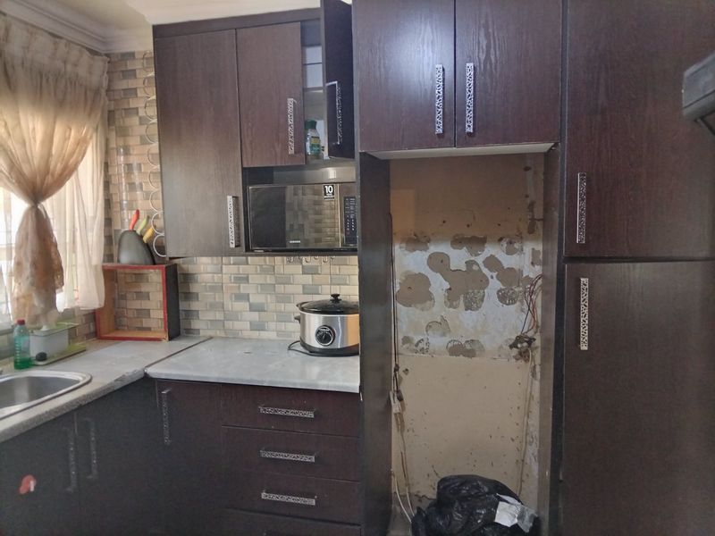 A kitchen featuring dark wood cabinetry and tiled backsplash, currently requiring repairs to the wall and appliance housing area.