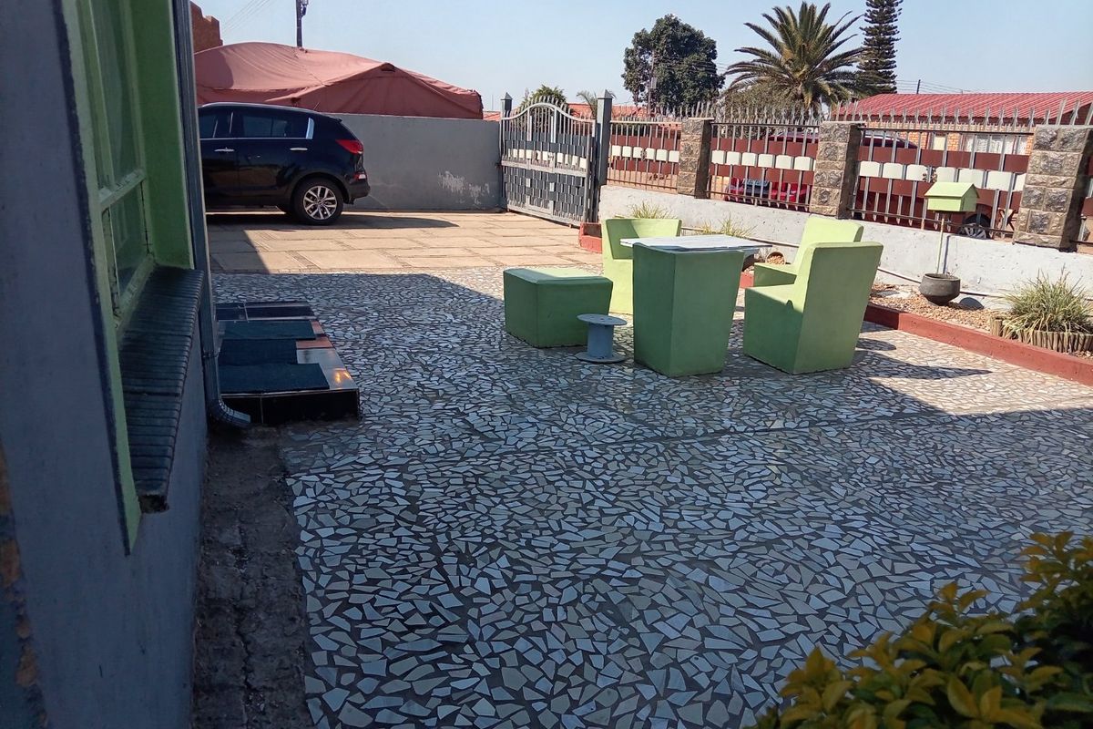 A paved rear courtyard area featuring a boundary wall with metal gate access and stone cladding details.