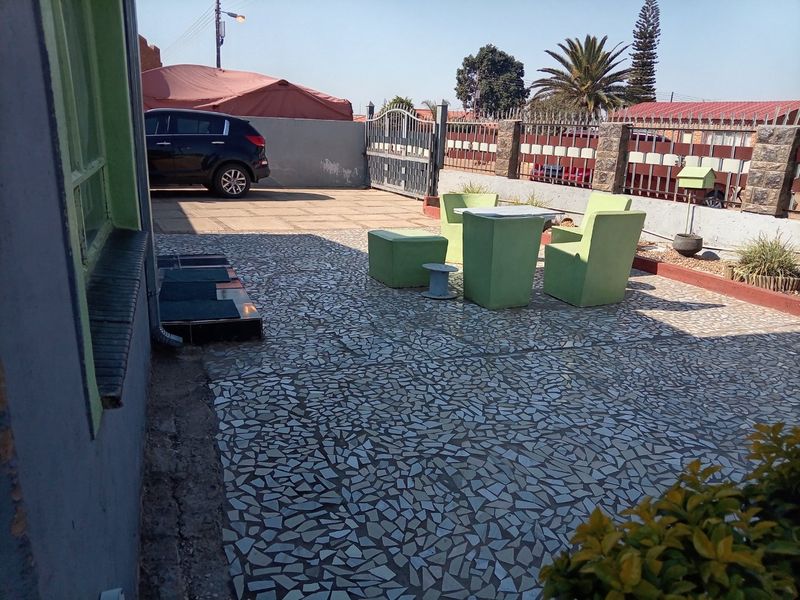 A paved rear courtyard area featuring a boundary wall with metal gate access and stone cladding details.