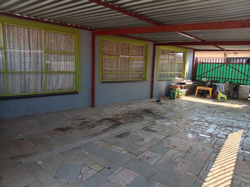 A covered outdoor patio area featuring tiled flooring, steel roofing, and security-barred windows, offering a functional space for outdoor living.