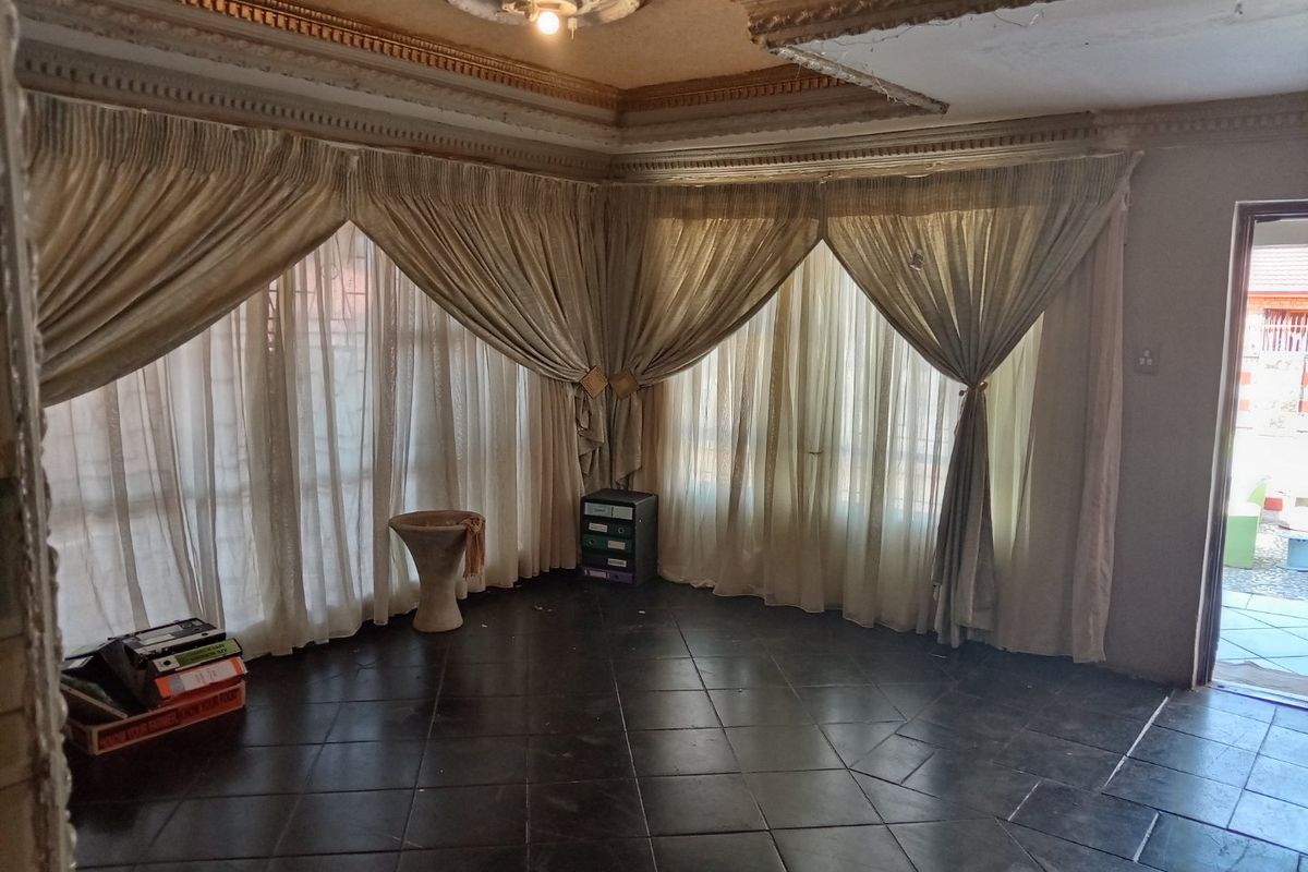 Spacious living area featuring ornate ceiling cornicing, a central ceiling rose, and dark tiled flooring with large windows allowing natural light.